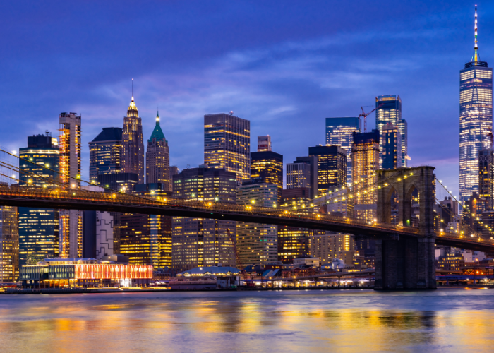Brooklyn bridge lit up at night above water.