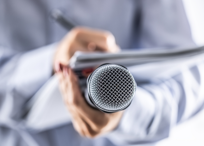 Journalist holding microphone taking notes on paper with pen while giving interview.
