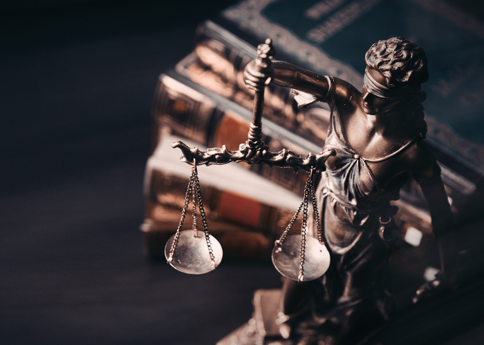 Gold figure of lady justice on desk next to books of multiple colors.