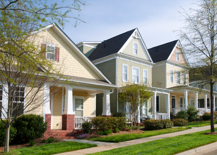 Three house in suburban neighborhood with bright green grass and bushes.