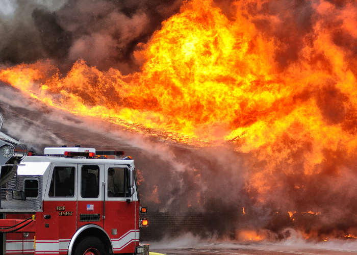 Firetruck parked in front of large blazing fire.