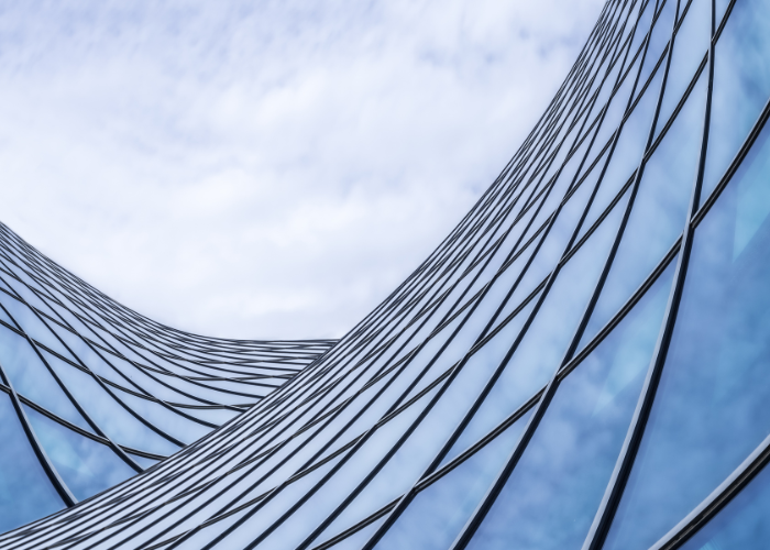 Curved glass windows against blue sky with clouds.